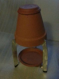 a small brown pot sitting on top of a metal stand next to a white wall