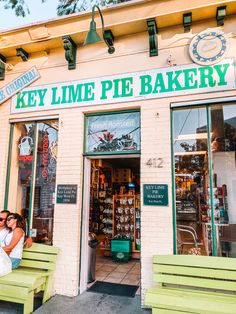 two people sitting on green benches in front of a bakery with their arms around each other