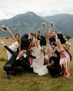 a large group of people posing for a photo in the grass with their hands up