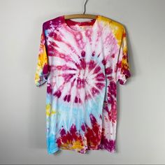 a colorful tie - dyed shirt hanging on a clothes hanger against a white wall