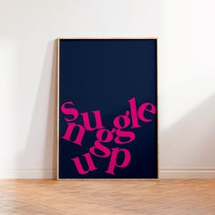 a poster with the words suggle up in pink on a dark blue background next to a wooden floor