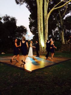 a group of people standing on top of a wooden floor in front of a tree