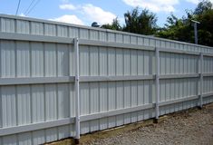 a white fence is next to gravel and trees