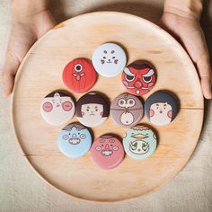 a person holding a wooden plate with six different buttons in the shape of faces on it