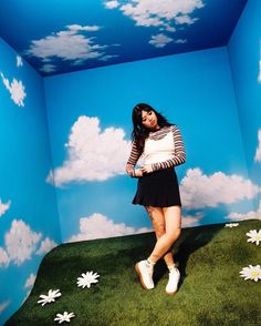 a woman standing in a room with clouds painted on the wall and grass growing all around