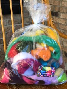 a plastic bag filled with lots of different colored yarns on top of a wooden table