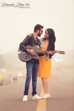 a man holding a guitar while standing next to a woman on the street with her arm around him