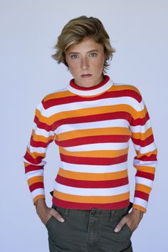 a woman in an orange and red striped sweater is posing for the camera with her hands on her hips