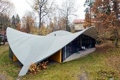 an unusual building in the middle of a forest with trees around it and grass on the ground