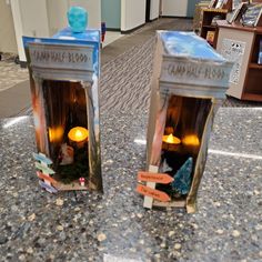 two small boxes with candles in them sitting on the ground next to bookshelves