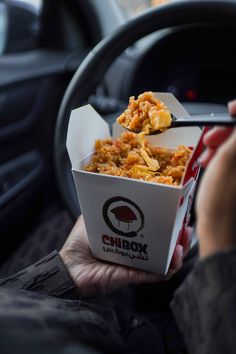 a person holding a box of food in their hand while sitting in a car with the steering wheel behind them