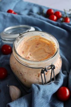 a glass jar filled with food sitting on top of a blue cloth next to tomatoes