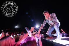 a man standing on top of a stage while holding his hands up to the crowd