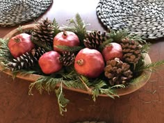 a wooden bowl filled with apples and pine cones on top of a table next to two place mats