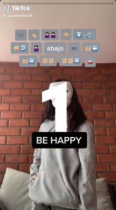 a woman standing in front of a brick wall with the words be happy on it