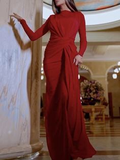 a woman in a long red dress standing next to a pillar with her hand on the wall