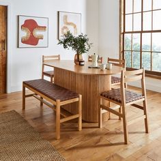 a dining room table with two chairs and a bench in front of the window, next to a potted plant