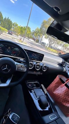 the interior of a mercedes benz car with its dashboard and steering wheel showing, there is a handbag on the dash