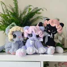 three crocheted kittens sitting on top of a white table next to a potted plant