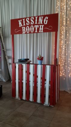 a red and white wooden booth with lights on the wall behind it that says kissing booth