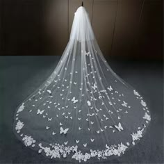 a wedding veil with white butterflies on the bottom is shown in front of a dark background