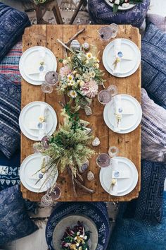 a wooden table topped with lots of white plates and flowers next to blue couches