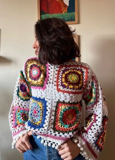 a woman standing in front of a wall wearing a colorful crochet granny sweater