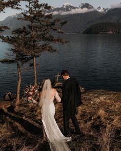 a bride and groom standing on the shore of a lake in front of some mountains