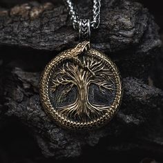 Yggdrasil and the Midgard Serpent, two symbols from the Nordic mythology that enliven this piece of Viking necklace. The Midgard Serpent, also known as Jormungand, surrounds the Norse tree of life called Yggdrasil that holds all possible worlds together. This necklace combines these two strands of Viking mythology in an exceptional design that will get you noticed in any crowd! The pendant is made from antique gold and has a highly distinct design. It makes for an excellent addition to any colle Gold Viking Style Jewelry, Viking Style Bronze Jewelry Gift, Handmade Viking Style Necklaces, Handmade Viking Round Necklace, Handmade Viking Style Round Necklaces, Handmade Viking Round Necklaces, Viking Style Engraved Round Pendant Necklace, Engraved Bronze Nature-inspired Jewelry, Nature-inspired Engraved Bronze Jewelry