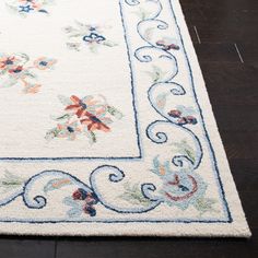 a white rug with blue trimmings and flowers on the bottom is sitting on a wooden floor