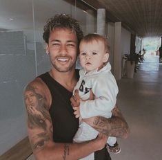 a man holding a baby in his arms and smiling at the camera with tattoos on his arm