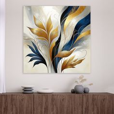 an abstract painting with gold and blue leaves on a white wall above a wooden cabinet