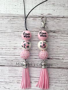 two pink and white beads with tassels are hanging from a string on a wooden surface