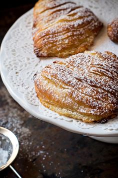 three croissants on a white plate covered in powdered sugar