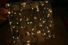 someone is holding up a string of lights in front of a wire mesh structure that has been wrapped around it