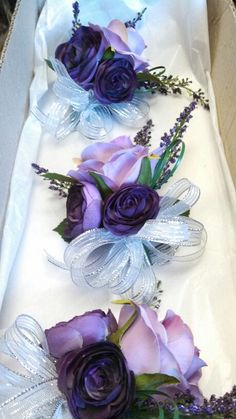 three purple flowers in a white box with ribbons and bows on the bottom one flower