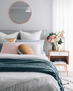 a bed with white sheets and pillows in a bedroom next to a round mirror on the wall