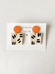 an orange and white square shaped earrings with black dots on the front, sitting on top of a card