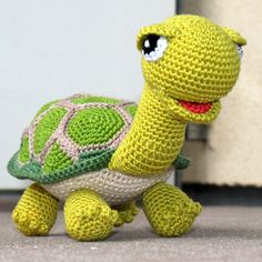 a small crocheted turtle sitting on the ground next to a door way with its eyes wide open