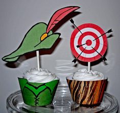 two cupcakes with paper birds on top of them, one has a target and the other has an arrow