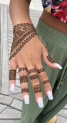 a woman's hand with henna tattoos and white nails on her left hand