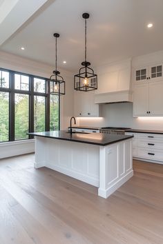 a large kitchen with an island in front of two windows and lights hanging from the ceiling