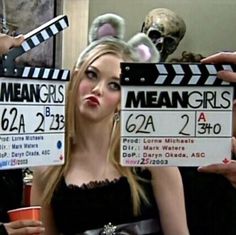 a woman holding up a clap board with the words mean girls on it in front of her face