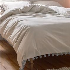 an unmade bed with white sheets and pom poms