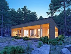 a small cabin is lit up at night in the woods with rocks and trees surrounding it