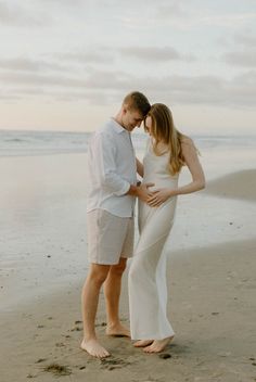 a pregnant couple standing on the beach with their hands around each other's waist