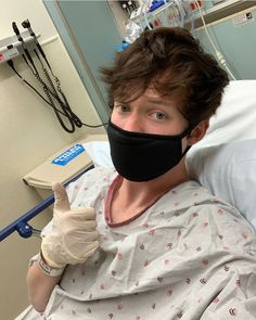 a man in a hospital bed wearing a face mask and gloves with his thumb up