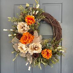 an orange and white wreath is hanging on the front door with pine cones, dried flowers, and greenery