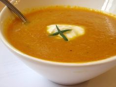 a white bowl filled with carrot soup on top of a table next to a spoon