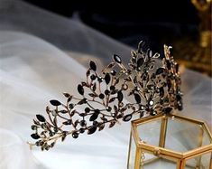 two tiaras sitting next to each other on a white cloth covered table with a gold box